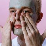 Jeune homme appliquant un masque pour le visage dans le cadre d'une routine de soins de la peau sur fond rose