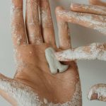 Détail rapproché de mains appliquant de l'argile blanche sur la peau, montrant la texture et les détails.