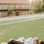 Un couple joyeux se détend sur une pelouse verte devant une charmante maison rustique le jour de leur mariage.