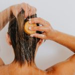 Dos d'une femme se lavant les cheveux sous la douche avec de l'eau qui coule.