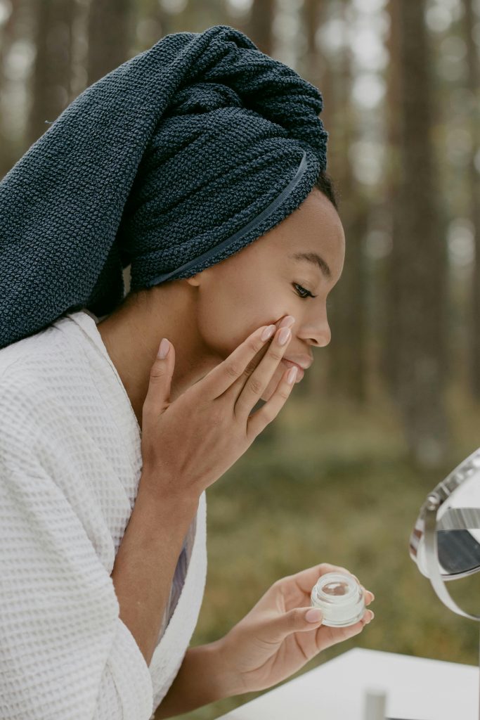 Woman profitant d'une routine de soins de la peau dans un cadre forestier, appliquant de la crème avec une concentration sereine