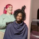 Positive African American female hairdresser coiffant un client masculin afro-américain dans un studio avec un mur rose clair
