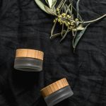 Organic cosmetic jars with wooden lids on black fabric and olive branches, vue de dessus