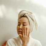 Asian woman applying facial cream at home in a relaxed setting, promoting beauty and skincare routines. Femme asiatique appliquant de la crème pour le visage à la maison dans un cadre détendu, promouvant les routines de beauté et de soins de la peau.