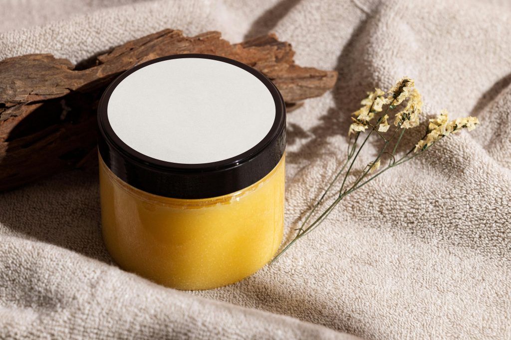 Jar of yellow skincare cream on a towel with wood and dried flowers, ideal for spa themes. Pot de crème de soin jaune sur une serviette avec du bois et des fleurs séchées, idéal pour les thèmes spa.