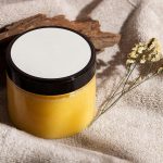 Jar of yellow skincare cream on a towel with wood and dried flowers, ideal for spa themes. Pot de crème de soin jaune sur une serviette avec du bois et des fleurs séchées, idéal pour les thèmes spa.