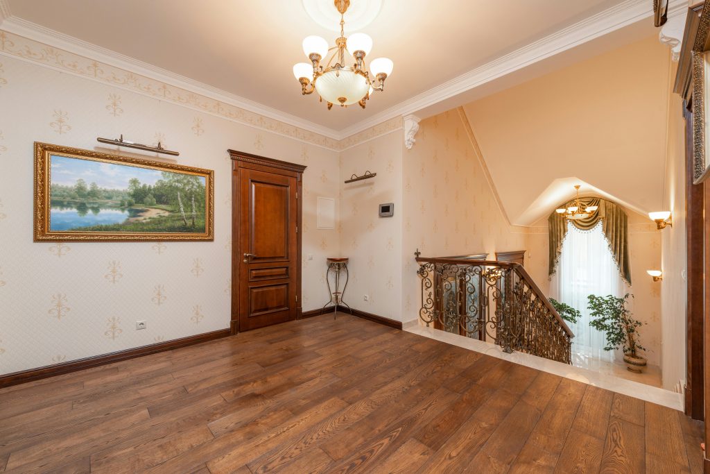 Spacious home interior showcasing elegant staircase, chandelier, and wooden floor. Intérieur spacieux mettant en avant un escalier élégant, un lustre et un parquet en bois.