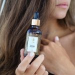 Woman with long hair holding a luxurious argan oil bottle. Ideal for beauty and skincare promotions. Femme aux cheveux longs tenant une bouteille d'huile d'argan luxueuse. Idéale pour les promotions de beauté et de soins de la peau.