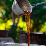 Close-up of golden liquid being poured outdoors with bokeh background. Gros plan d'un liquide doré versé à l'extérieur avec un arrière-plan flou.