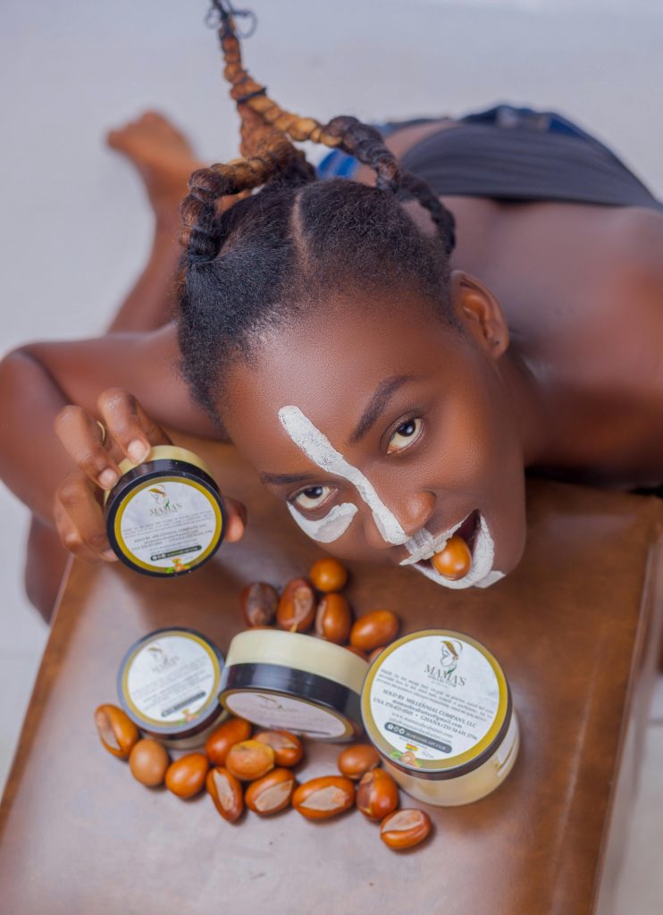 African woman biting nut, posing with natural shea skincare products and cream jars. Femme africaine mordant une noix, posant avec des produits de soin à base de karité naturel et des pots de crème.