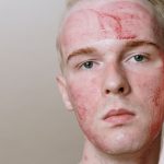 Close-up of a man with red skincare treatment mask, emphasizing healthy skin and self-care. Gros plan d'un homme portant un masque de traitement de soin de la peau rouge, mettant l'accent sur une peau saine et l'auto-soin.