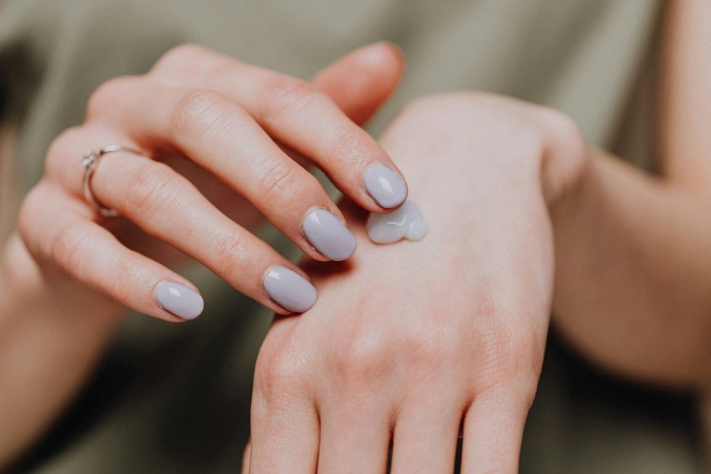 Femme méconnaissable en chemise décontractée avec manucure tendance et bague appliquant de la crème pour les mains à l'arrière de la peau de la main