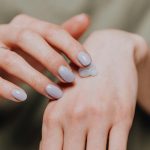 Femme méconnaissable en chemise décontractée avec manucure tendance et bague appliquant de la crème pour les mains à l'arrière de la peau de la main