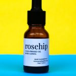 Close-up of rosehip oil bottle with vibrant yellow and blue backdrop. Gros plan d'une bouteille d'huile d'églantier avec un fond jaune vif et bleu vibrant.
