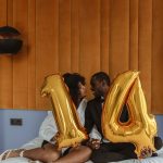 Couple assis intimement sur un lit tenant des ballons dorés numéro 14, célébrant l'amour.