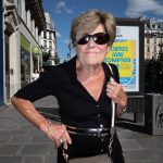 Elderly woman wearing sunglasses posing confidently on a bustling city sidewalk. Femme âgée portant des lunettes de soleil posant avec confiance sur un trottoir animé d'une ville.