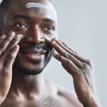 Homme souriante appliquant une crème pour le visage dans le cadre de sa routine de soins de la peau quotidienne pour une peau saine.