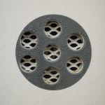 Detailed view of a wet metal drain cover with water droplets and textured surface. Vue détaillée d'une grille d'égout métallique mouillée avec des gouttelettes d'eau et une surface texturée.