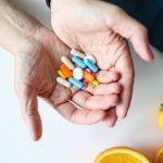 Close-up of hands holding multicolored pills with oranges, symbolizing health and nutrition. Gros plan de mains tenant des pilules multicolores avec des oranges, symbolisant la santé et la nutrition.